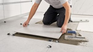 tile flooring installation cost — professional installer placing large-format porcelain tiles with spacers and notched trowel